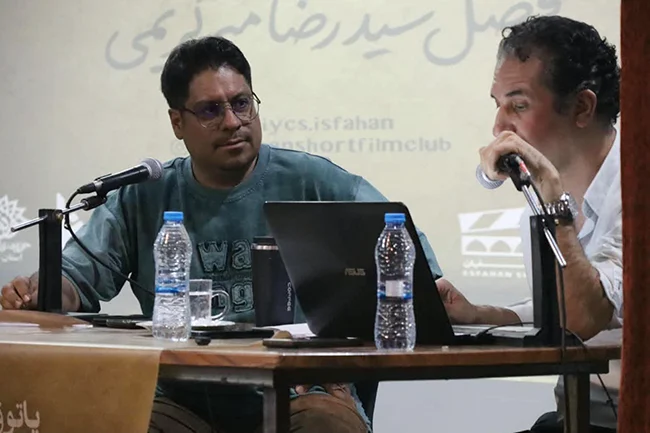نشست تخصصی «استعاره در فیلم کوتاه» در پاتوق ۱۴۰ فیلم کوتاه اصفهان با حضور دکتر سیاوش گلشیری، نویسنده و پژوهشگر سینما، برگزار شد. در این جلسه چهار فیلم «هلیوس» به کارگردانی مجید صداقت برجی و سارا طالبیان، «صوراحیل» ساخته اسماعیل عظیمی، «جاذبه غیرنیوتونی» اثر علیرضا صادقی و «مرخ» به کارگردانی حسین فیروزه نمایش داده شد و آثار از منظر ساختار روایی، شخصیت‌پردازی، ایده محرک و کارکرد استعاره مورد بررسی قرار گرفتند. تفاوت‌های بنیادین فیلم کوتاه و بلند محمد بزرگ، میزبان این نشست، ضمن خوشامدگویی به سیاوش گلشیری، بر اهمیت بحث فیلم‌نامه در جلسات پاتوق تأکید کرد و حضور فیلم‌سازان و پژوهشگران در این نشست‌ها را فرصتی برای تبادل تجربه و گفت‌وگو درباره سینما دانست. گلشیری در آغاز سخنان خود با اشاره به سابقه فعالیتش در انجمن سینمای جوانان، بر تفاوت سازوکار فیلم کوتاه و فیلم بلند تأکید کرد و گفت فیلم کوتاه را نباید نسخه فشرده‌ای از فیلم بلند دانست. به گفته او، فیلم کوتاه سازوکار مستقل خود را دارد و معمولاً بر پایه یک ایده واحد، شخصیت‌های محدود، زمان و مکان فشرده و یک کنش دراماتیک مشخص شکل می‌گیرد؛ کنشی که در بسیاری از موارد با یک ضربه نهایی به پایان می‌رسد. ایده محرک؛ نقطه آغاز روایت کوتاه این پژوهشگر سینما با بررسی فیلم‌های نمایش‌داده‌شده، ضعف در شکل‌گیری کنش دراماتیک و ارتباط میان اجزای روایت را از جمله چالش‌های برخی آثار دانست. او «ایده محرک» را یکی از عناصر کلیدی فیلم‌نامه کوتاه معرفی کرد؛ ایده‌ای که باید شخصیت اصلی و مسئله فیلم را شکل دهد و در ادامه به‌صورت منطقی به پایان اثر متصل شود. گلشیری با اشاره به فیلم کوتاه «اتاق ۸»، آن را نمونه‌ای از پیوند میان ایده محرک، کنش شخصیت و ضربه نهایی دانست و تأکید کرد که اتفاقات پایانی باید از منطق درونی روایت ناشی شوند و صرفاً به‌صورت تصادفی وارد جهان فیلم نشوند. منطق شخصیت؛ پرهیز از کنش‌های تحمیلی گلشیری با اشاره به فیلم‌هایی مانند «روتوش» و «انیمال»، بر ضرورت طراحی درست کنش شخصیت تأکید کرد. به گفته او، رفتار شخصیت باید بر اساس نیاز و منطق درونی او شکل بگیرد، نه صرفاً بر مبنای تصمیم فیلم‌نامه‌نویس. او همچنین نبود تناسب میان انگیزه، ایده محرک و ضربه نهایی را از ایرادهای رایج در فیلم‌های کوتاه دانست و گفت چنین مسئله‌ای می‌تواند روایت را به سمت اتفاقات تصادفی و غیرقابل باور سوق دهد. استعاره در فیلم کوتاه؛ معنا در دل تصویر در بخش اصلی این نشست، موضوع «استعاره در فیلم کوتاه» مورد بررسی قرار گرفت. گلشیری با اشاره به جایگاه استعاره در هنر مدرن و پست‌مدرن توضیح داد که هنرمند می‌تواند به جای بیان مستقیم دیدگاه خود، از عناصر استعاری و شاعرانه برای انتقال معنا استفاده کند. او با اشاره به برخی نمونه‌های فیلم کوتاه ایرانی و خارجی، از جمله «روتوش»، «هستی»، «انیمال» و «دولباگ» ساخته کریستوفر نولان، گفت در بسیاری از این آثار، امر ناگفته بر امر تصریح‌شده غلبه دارد و معنا از طریق کنش‌ها، تصاویر و عناصر بصری شکل می‌گیرد. گلشیری تأکید کرد که استعاره زمانی در فیلم موفق عمل می‌کند که در متن اثر ساخته شود و صرفاً به عنوان فیلم یا استفاده از یک نماد کلیشه‌ای محدود نماند. او با اشاره به مثال «کبوتر سفید» توضیح داد که یک عنصر تصویری لزوماً معنای ثابت و قراردادی ندارد و معنای استعاری آن باید در بستر جهان و تجربه خود اثر شکل بگیرد. نقش عناصر بصری در شکل‌گیری استعاره گلشیری در ادامه بر نقش عناصر بصری در خلق استعاره سینمایی تأکید کرد و گفت استعاره می‌تواند از طریق نور، رنگ، لباس، میزانسن، ترکیب‌بندی، صدا و شیوه تدوین شکل بگیرد. او همچنین با اشاره به مقاله «شیوه‌های بیان در سینما» نوشته دکتر احمد ضابطی جهرمی، مطالعه این مقاله و تماشای نمونه‌های مطرح‌شده در نشست را برای علاقه‌مندان به سینما و فیلم کوتاه پیشنهاد کرد. این نشست با گفت‌وگو درباره نمونه‌های مطرح‌شده و پاسخ به پرسش‌های حاضران به پایان رسید.